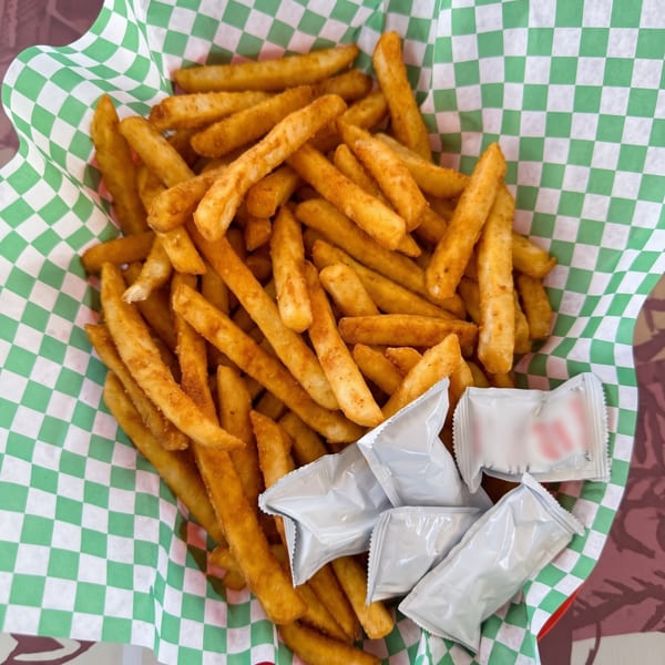 A basket of seasoned french fries in green and white checkered paper with ketchup packets.