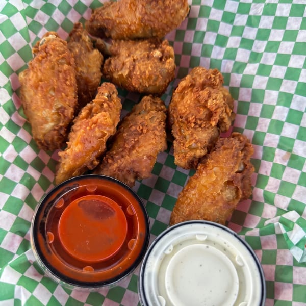 Crispy fried chicken wings in a green and white checkered basket with two dipping sauces.